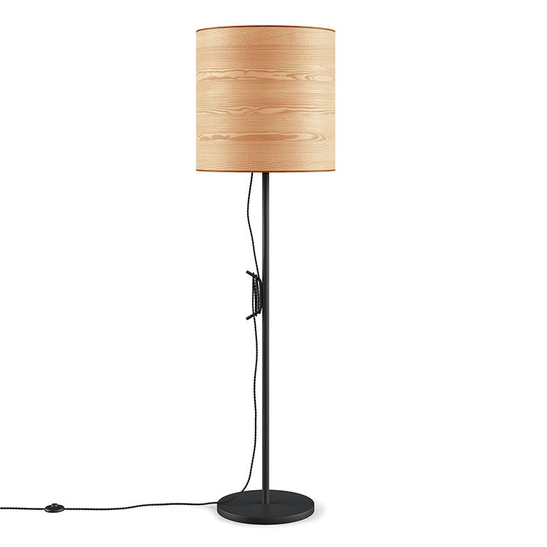 Floor lamp with a light woodgrain drum shade and a slim black metal base, featuring a visible cord and switch.