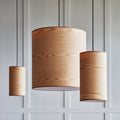 Three wood veneer pendant lights hanging against a white paneled wall with black cords