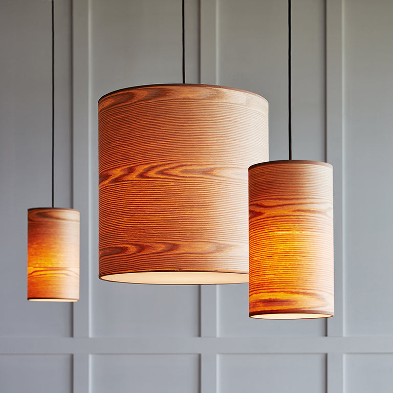 Three large pendant lights with warm wood grain shades hanging in front of a paneled gray wall