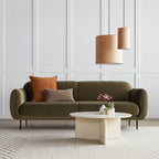 Two wood veneer pendant lights hanging above a modern olive green sofa with decorative pillows and a round coffee table