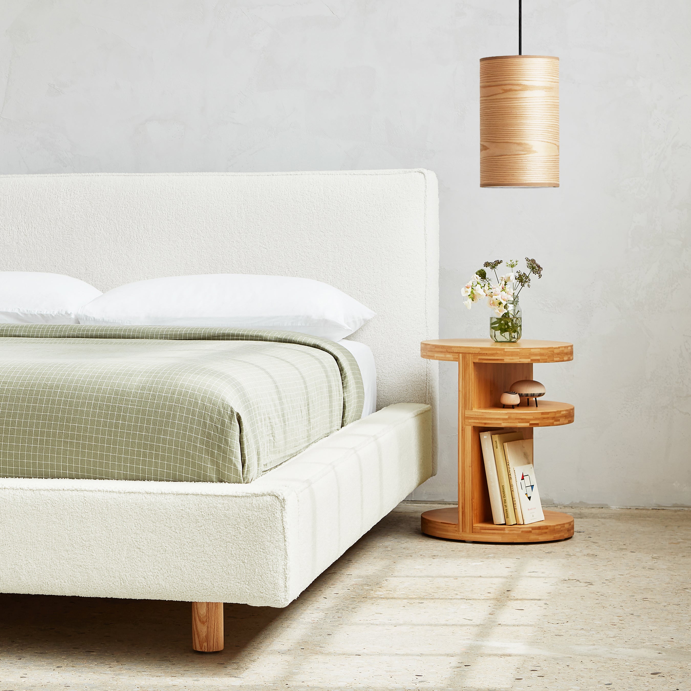 Small wooden pendant light with ash veneer hanging above a modern wooden side table next to a bed with light upholstery