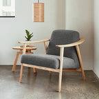 Modern midcentury style armchair with gray cushions and light wood frame next to a small wooden side table and pendant light