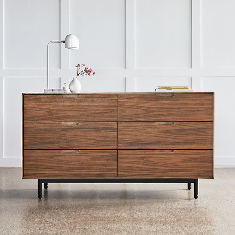 Modern six-drawer walnut dresser with sleek handles and black metal legs in a minimalist room setting