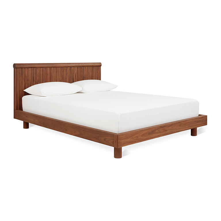 Mid-century modern wooden bed frame with a slatted headboard and white bedding and pillows.
