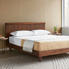 Modern wooden bed frame with vertical slatted headboard, white bedding, beige throw, and neutral bedroom decor