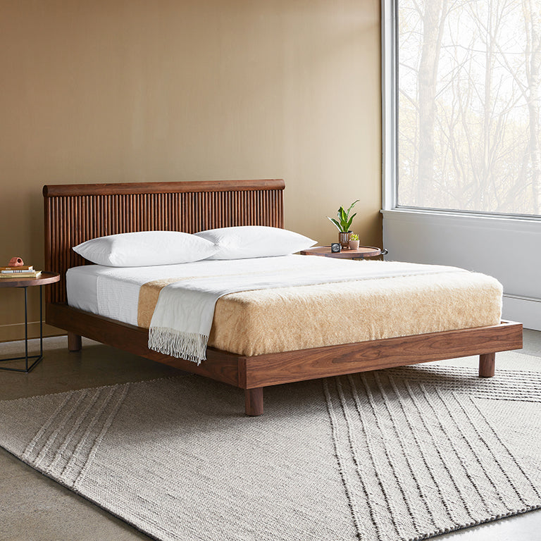 Modern wooden bed with slatted headboard, neutral bedding, and minimalist bedroom decor near large window