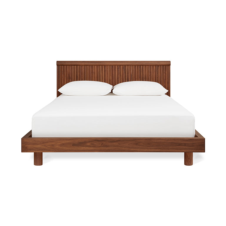 Midcentury modern walnut wood bed frame with slatted headboard and white bedding, minimalistic design