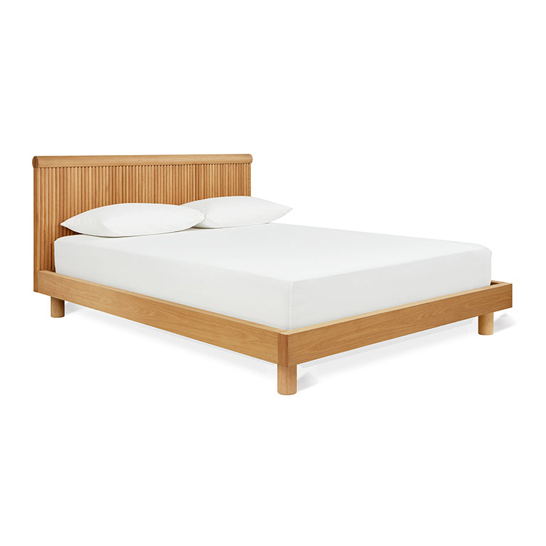 Wooden bed frame with slatted headboard in natural finish, styled with white bedding and pillows.