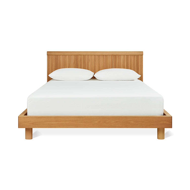 Modern wooden bed frame with slatted headboard and white bedding in a minimalist style