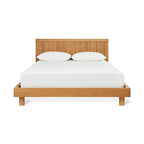 Modern wooden bed frame with slatted headboard and white bedding in a minimalist style