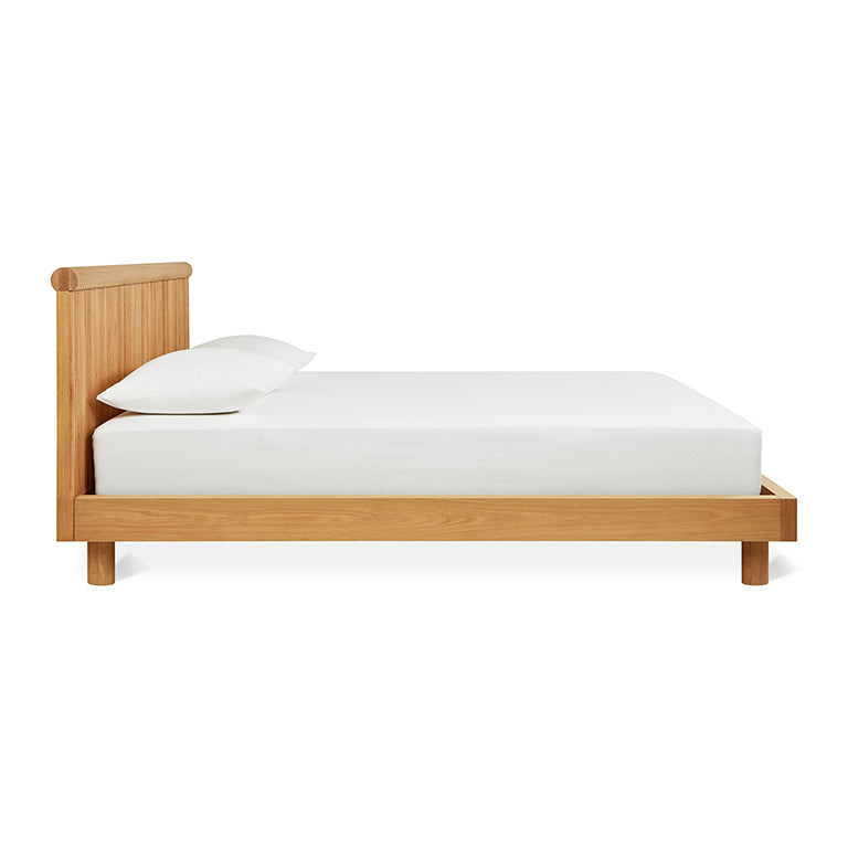 Minimalist wooden bed frame with a natural oak finish and a simple white mattress and pillow