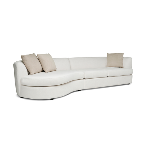 Curved white upholstered sectional sofa with beige pillows and modern design on low black legs.