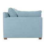 Side view of a light blue denim fabric sofa with wooden legs and plush cushions