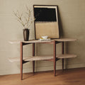 Minimalist travertine and oak console table with decorative vase, abstract framed artwork, and books on wooden floor.