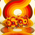 Two clear glasses with retro orange, red, and yellow swirl patterns on a matching colorful background