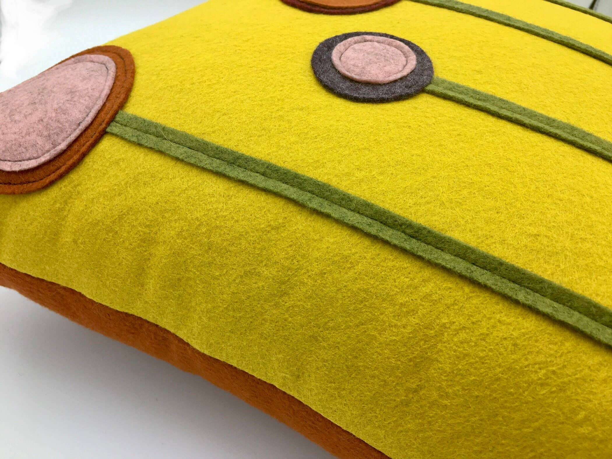 Close-up of a yellow wool felt pillow with decorative flower patterns in pink, green, and brown tones.
