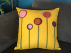 Yellow wool felt pillow with multicolored flower designs, placed on a dark gray couch for home decor.