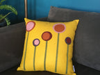 Yellow wool felt pillow with colorful abstract flower designs on a gray couch in a living room setting