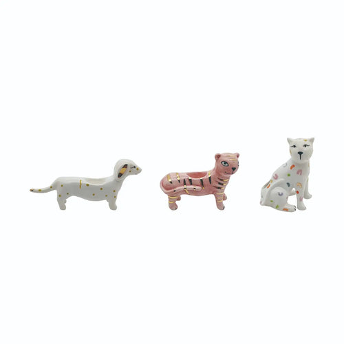 Three small ceramic animal figurines on a plain white background: a white dog with gold dots, a pink tiger with black stripes and a planter opening, and a white cat with multicolored spots.