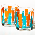 Pair of clear rocks glasses with bright blue and orange geometric patterns and white starburst accents