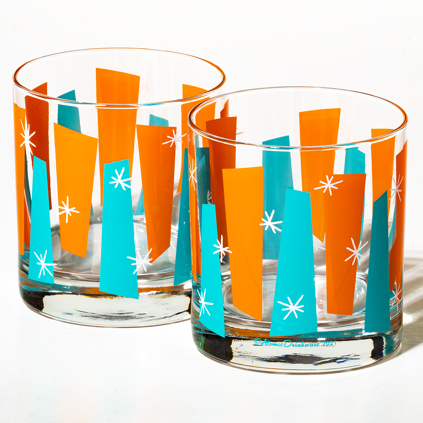 Pair of clear rocks glasses with bright blue and orange geometric patterns and white starburst accents