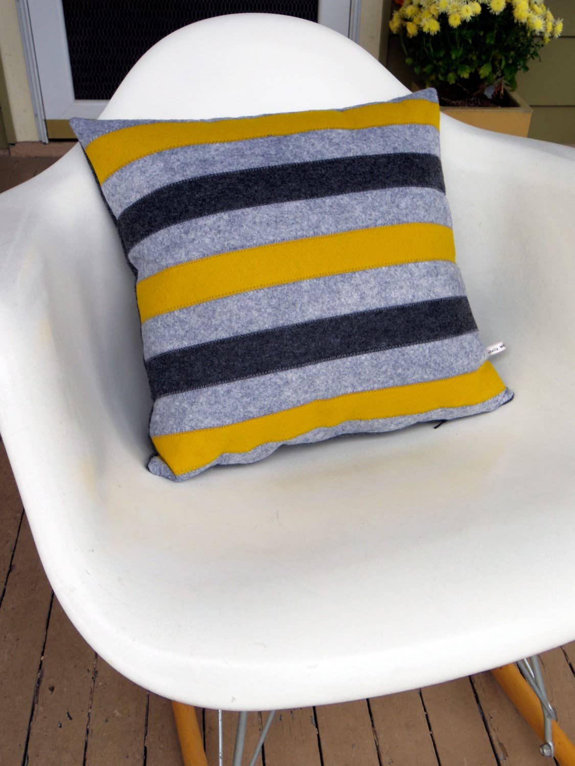 Striped wool felt pillow in gray, black, and mustard yellow resting on a modern white chair outdoors.