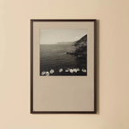 Framed black and white photograph of a coastal scene with boats on a beige wall.
