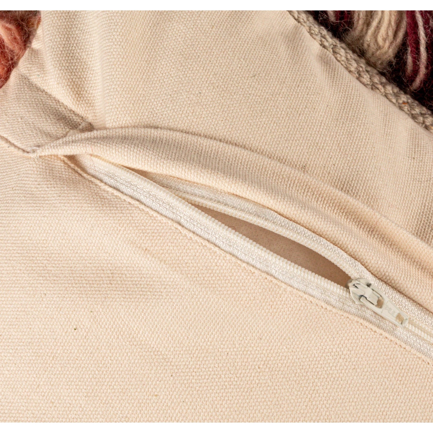 Close-up of a cream fabric pillow cover with a white zipper partially open on the back side.