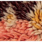 Close-up of multicolor wool shag fabric with textured fibers in orange, yellow, beige, and dark brown tones.