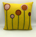 Bright yellow wool felt pillow with abstract flower designs in earthy tones and green stems on front surface