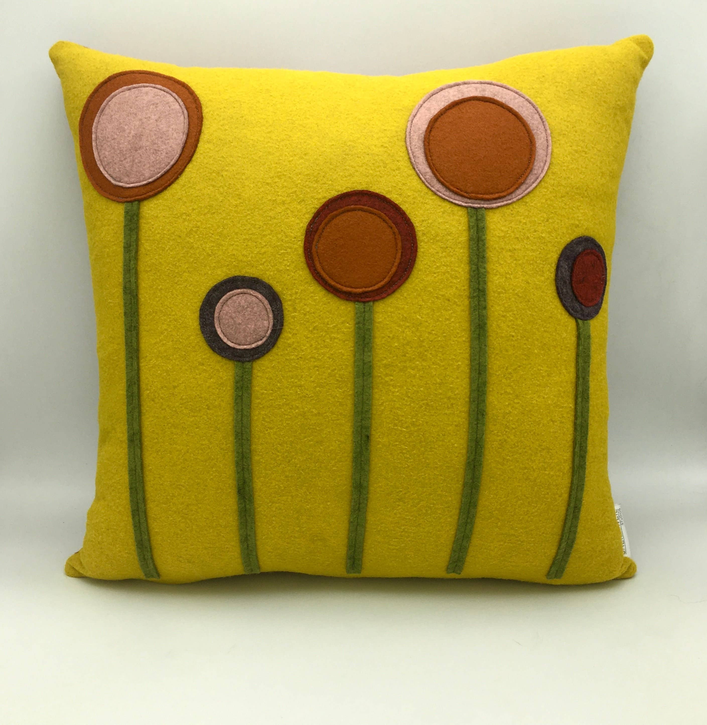 Bright yellow wool felt pillow with abstract flower designs in earthy tones and green stems on front surface