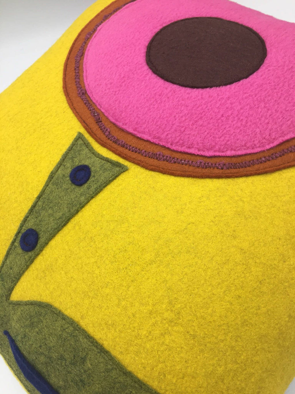 Close-up of a wool felt throw pillow with bright yellow, pink, brown, and green abstract flower design.