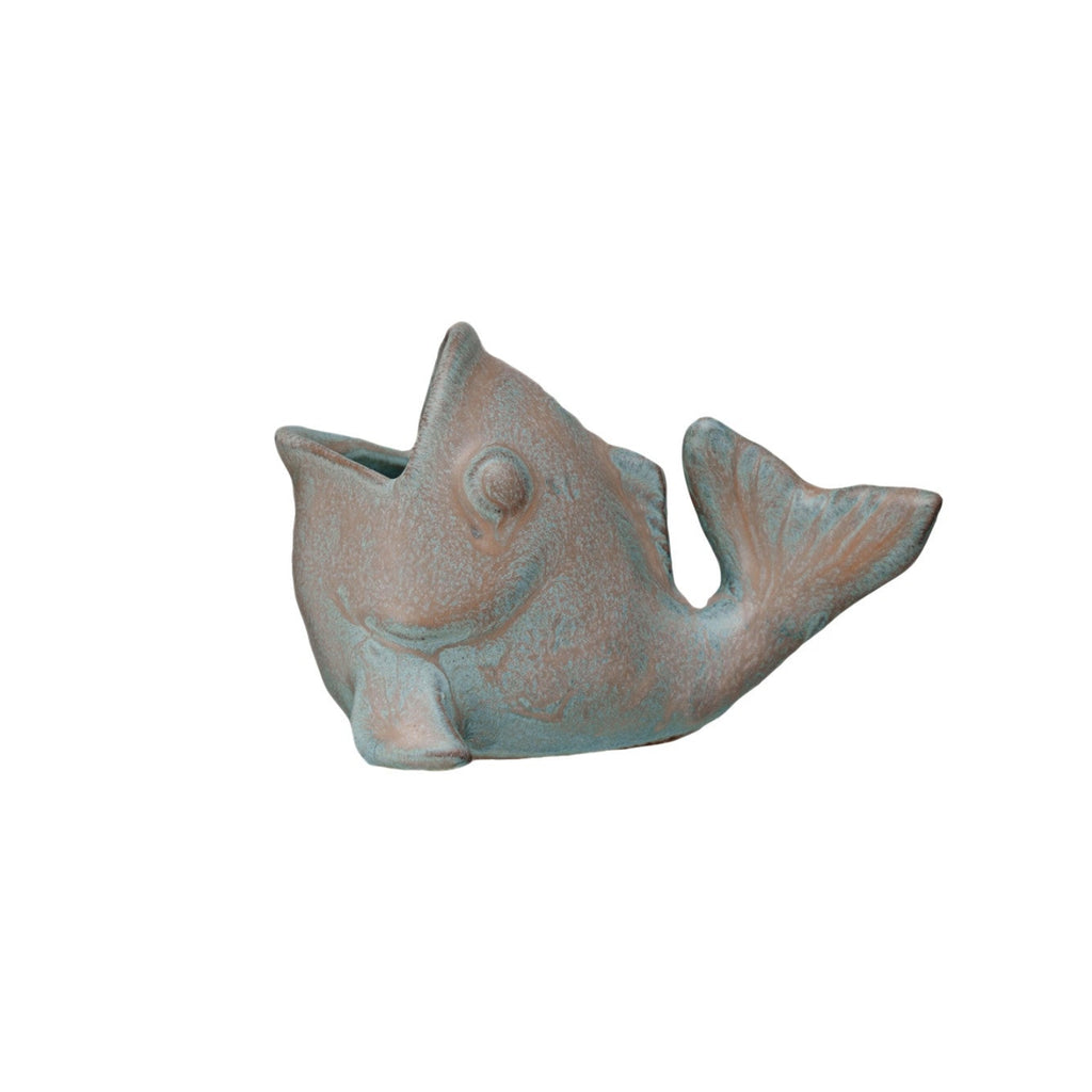 A small fish-shaped decorative object with a distressed metallic finish, featuring a mix of muted teal-blue and warm bronze-brown tones, isolated on a white background.