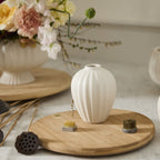 White vase on a wooden stand with flowers and decorative items in the background