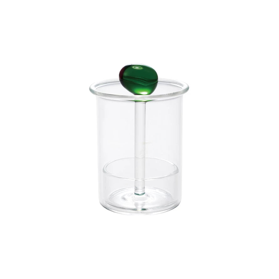 Clear glass toothpick holder with a green olive-shaped handle on top, minimalist home decor accessory.