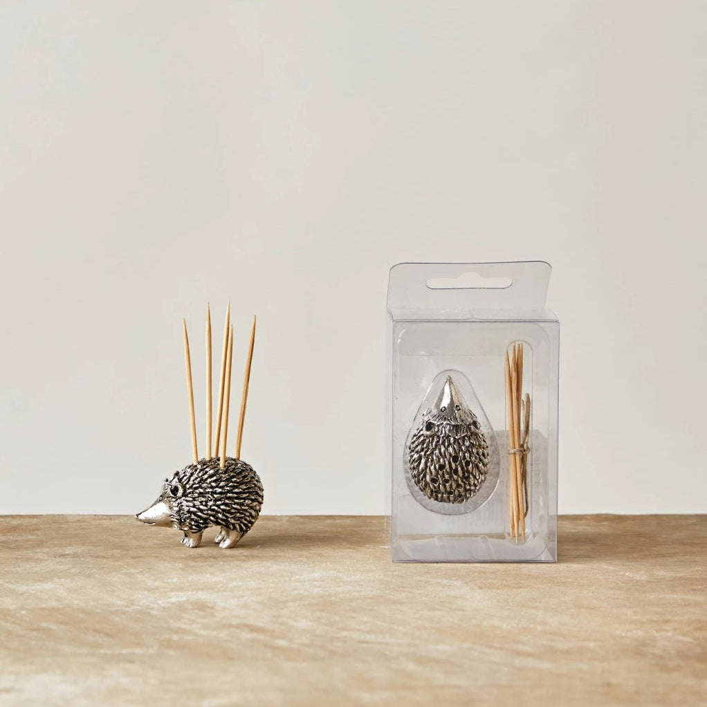 Small decorative hedgehog holding wooden toothpicks with a textured body, displayed next to packaged set on a wooden surface