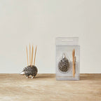 Small decorative hedgehog holding wooden toothpicks with a textured body, displayed next to packaged set on a wooden surface