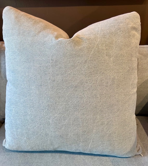 Soft textured light gray denim pillow with a plush, square shape placed on a couch cushion.