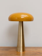 Yellow mushroom-shaped lamp with a brass tapered base on a wooden surface against a neutral background