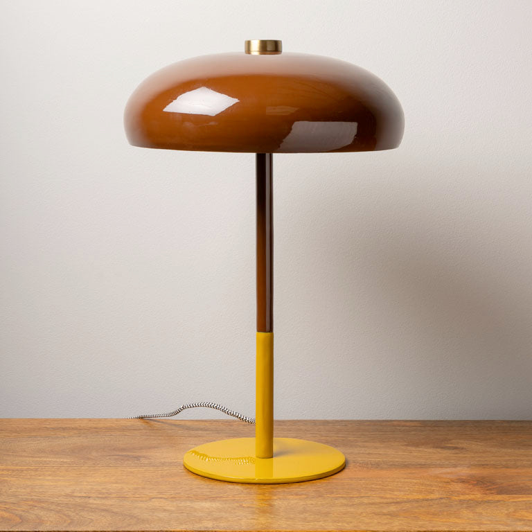 Modern table lamp with a glossy brown dome shade and yellow base on a wooden surface against a plain wall