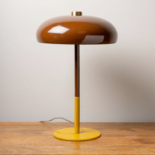 Modern table lamp with a glossy brown dome shade and yellow base on a wooden surface against a plain wall