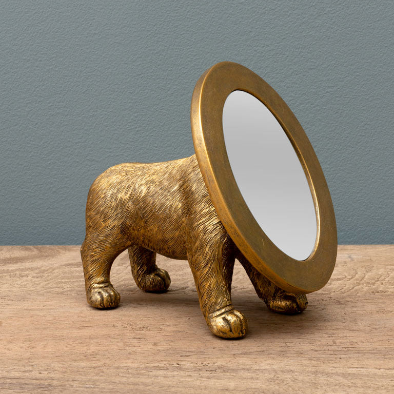 Decorative gold dog figurine with circular mirror replacing head, standing on wooden surface against blue wall.