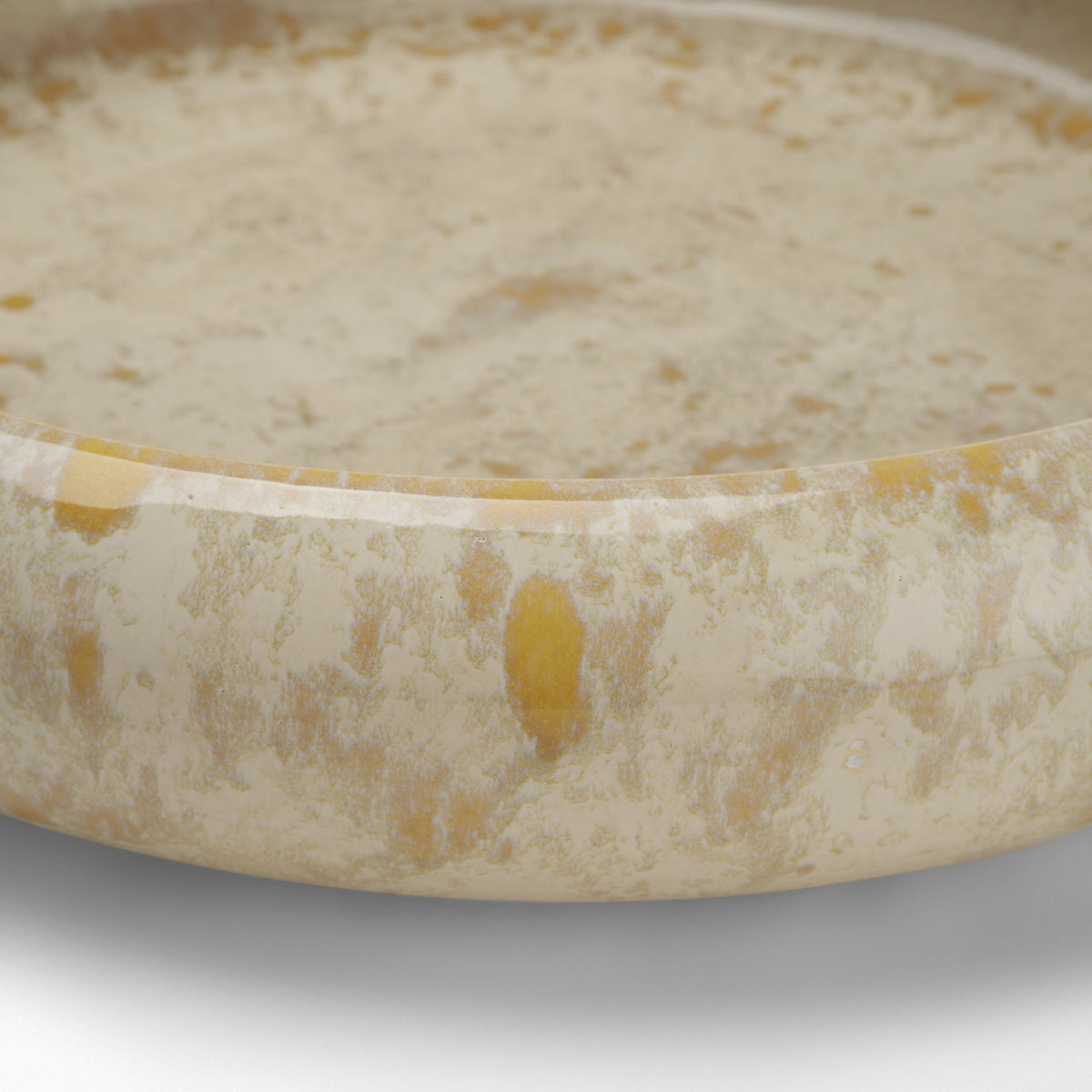 A close-up of a shallow round bowl or dish filled with a creamy off-white liquid or mixture, showing a marbled beige-and-cream surface with small yellowish inclusions.