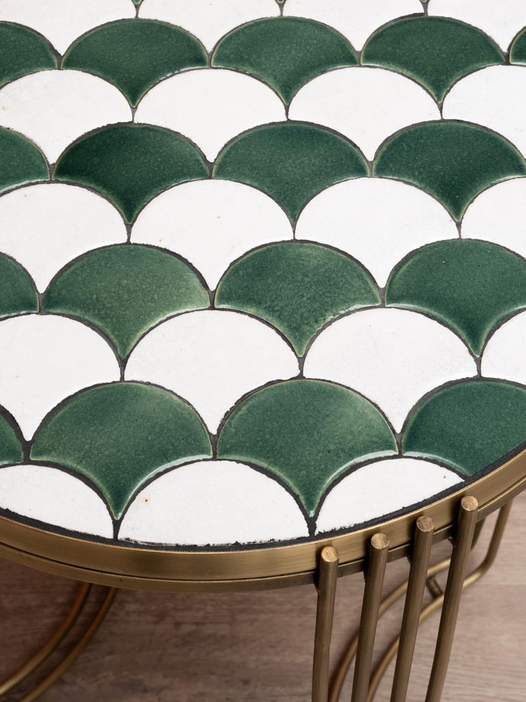Close-up of a round side table with green and white scalloped ceramic tile top and metal frame base.