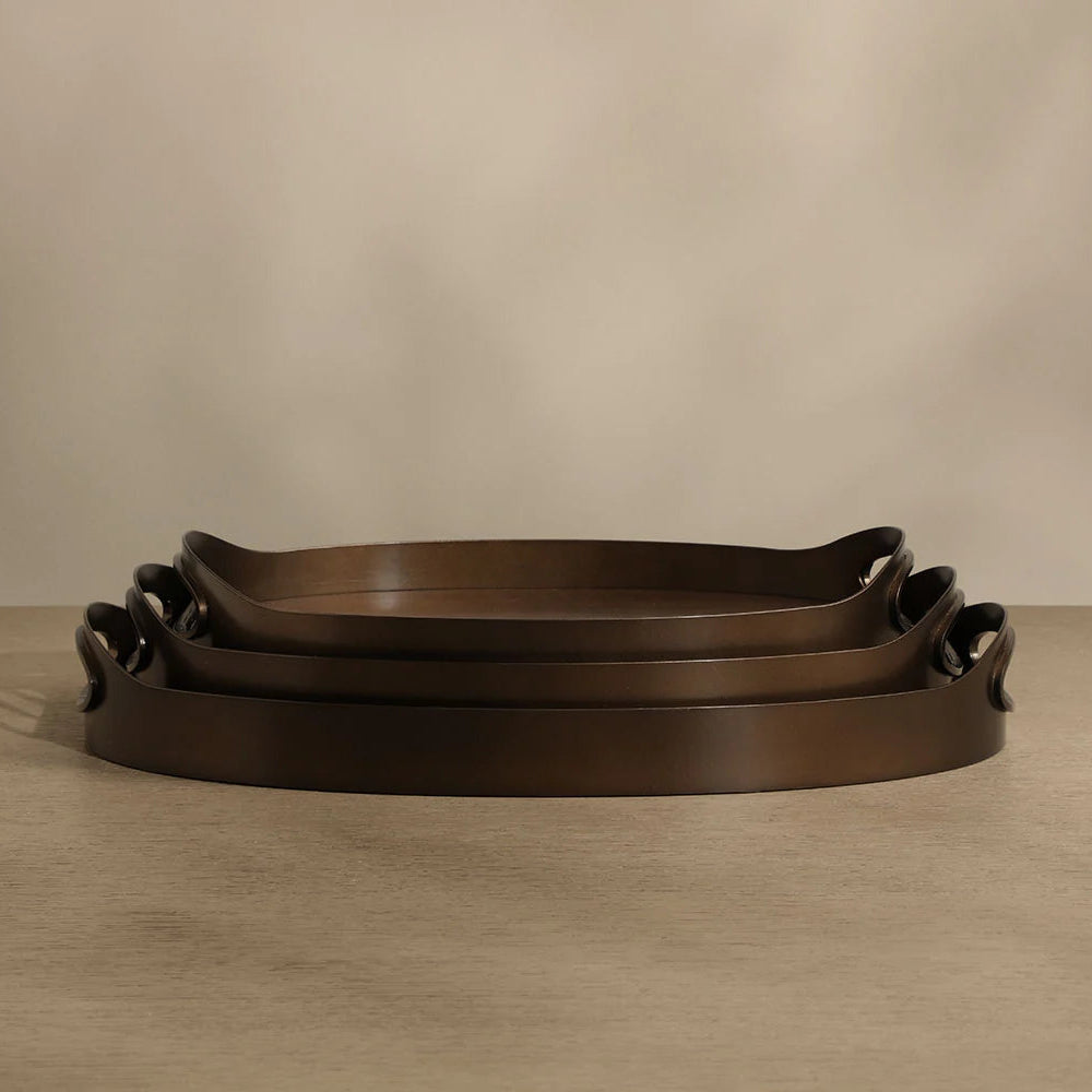 Set of three dark brown leather trays with handles on a beige background