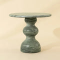 A round green marble side table with a sculptural, bulbous pedestal base, shown against a solid beige background.