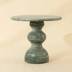 A round green marble side table with a sculptural, bulbous pedestal base, shown against a solid beige background.