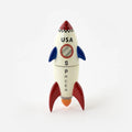 A small decorative toy rocket in a retro space theme, featuring a cream-colored body with red fins and nose cone, blue wings, and black text reading 'USA' and 'SPACE'.