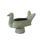 A ceramic bird-shaped planter shaped like a pigeon, featuring a textured glaze in muted blue-gray and brown tones with a small gold accent on the eye, set against a plain white background.