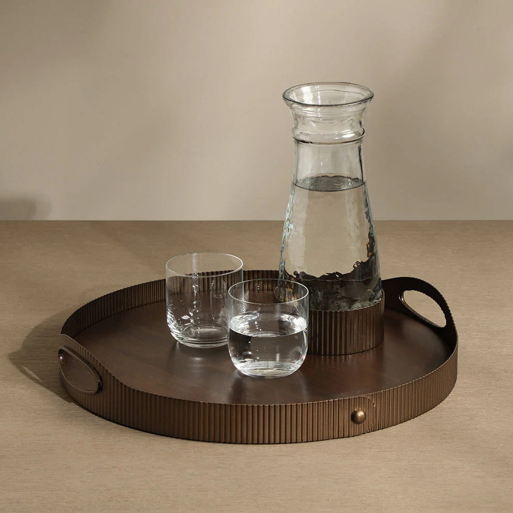 Glass carafe and two glasses on a wooden tray with a beige background